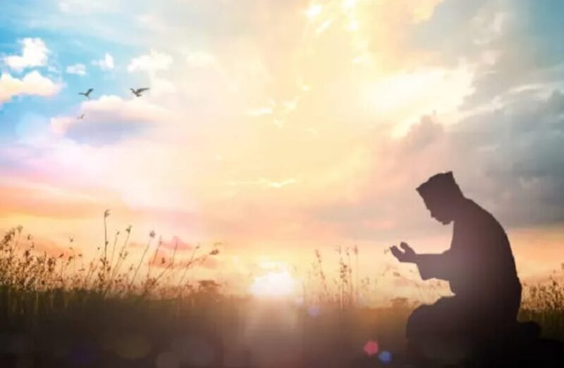 Momen ketenangan saat seseorang berdoa di tengah sinar mentari pagi.