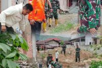 Personel TNI-AD Koramil 417-03/Air Hangat bersama warga Desa Baru Kubang bergotong royong membangun tanggul darurat menggunakan karung pasir untuk menahan luapan Sungai Batang Merao, Jumat (28/11/2025).