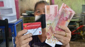 Seorang warga menunjukkan Kartu Keluarga Sejahtera (KKS) dan uang bantuan sosial yang diterima dari program pemerintah.